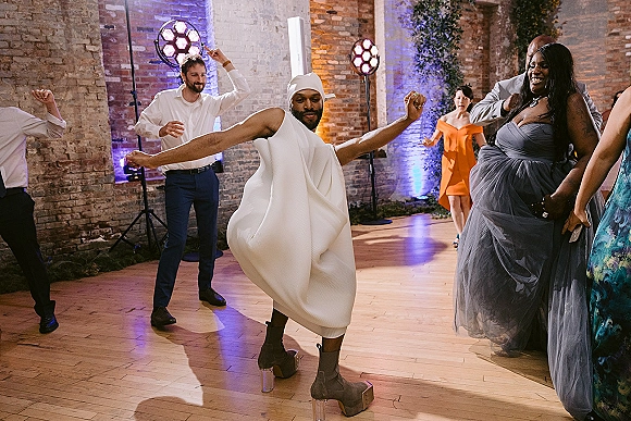 Wedding reception dancing as guests in formalwear celebrate on a lit dance floor with uplighting and stage lights against brick walls