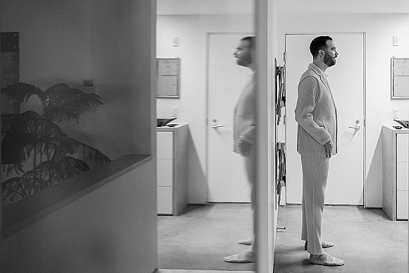 Groom portrait of a man in a striped suit with hands in pockets, standing in an indoor hallway by a doorway on tile floor