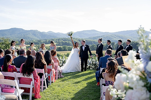 Ceremony recessional at an outdoor wedding ceremony as bride and groom walk up the aisle, bride raising bouquet overhead, mountains behind
