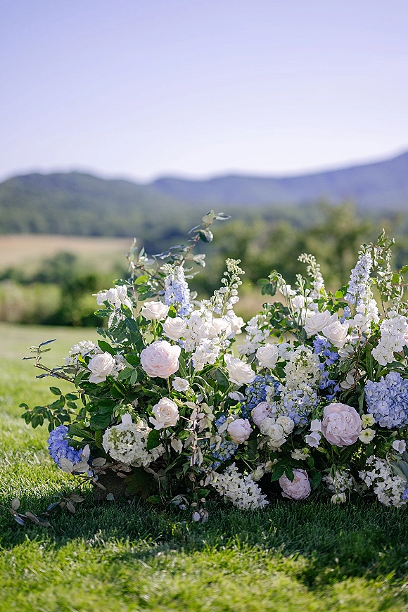 Wedding ceremony florals with ground altar flowers in roses, peonies, hydrangea and greenery on a grass lawn with rolling hills and mountains behind