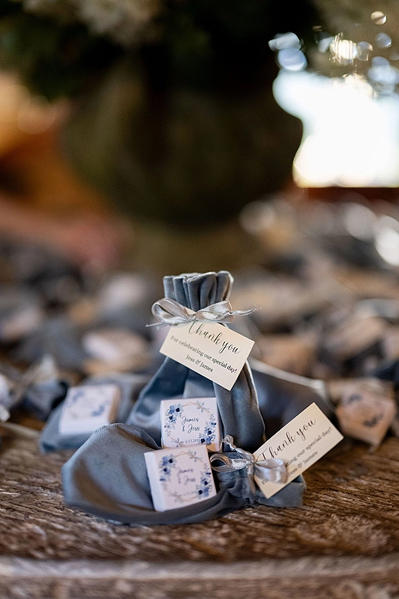 Wedding favors with thank you wedding tags on fabric bags and small boxes, tied with satin bows on a wood tabletop with bokeh lights