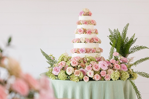 Wedding cake with tiered wedding cake design in white buttercream, topped with roses, carnations, hydrangea, and fern greenery on a linen table