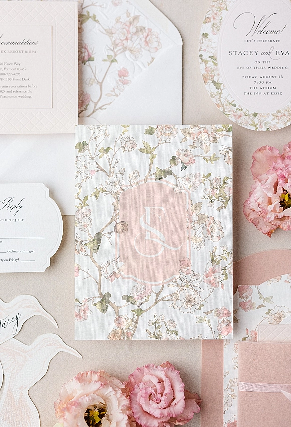 Invitation suite with floral wedding invitations, monogram and RSVP cards, die-cut place cards, blush ribbon, and pink flowers on neutral fabric backdrop