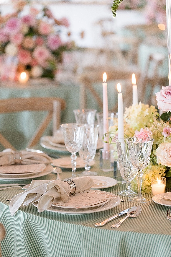 Reception tablescape with pastel wedding tablescape florals, taper and votive candles, crystal goblets, and menu cards in soft lighting