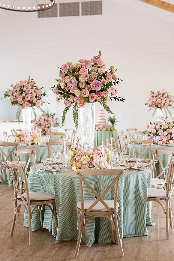 Wedding reception tablescape with mint green tablecloths, tall pink rose centerpieces, floating and taper candles, crystal place settings in a white tent
