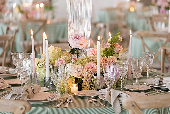 Reception tablescape with wedding table centerpiece of pastel roses and hydrangeas, taper candles, crystal glasses, and striped linen under bokeh lights