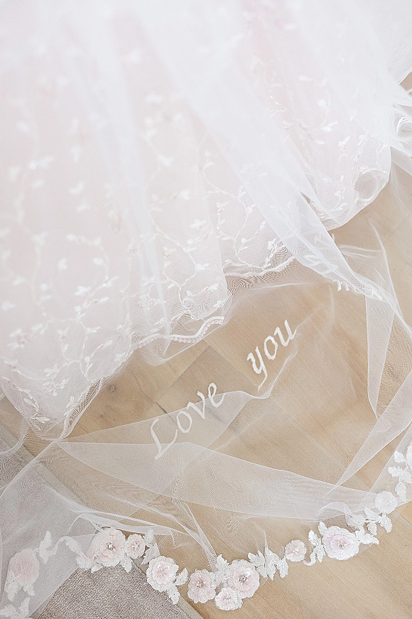 Wedding veil with personalized wedding veil embroidery, floral lace applique and soft tulle spread across a wood floor and carpet flat lay