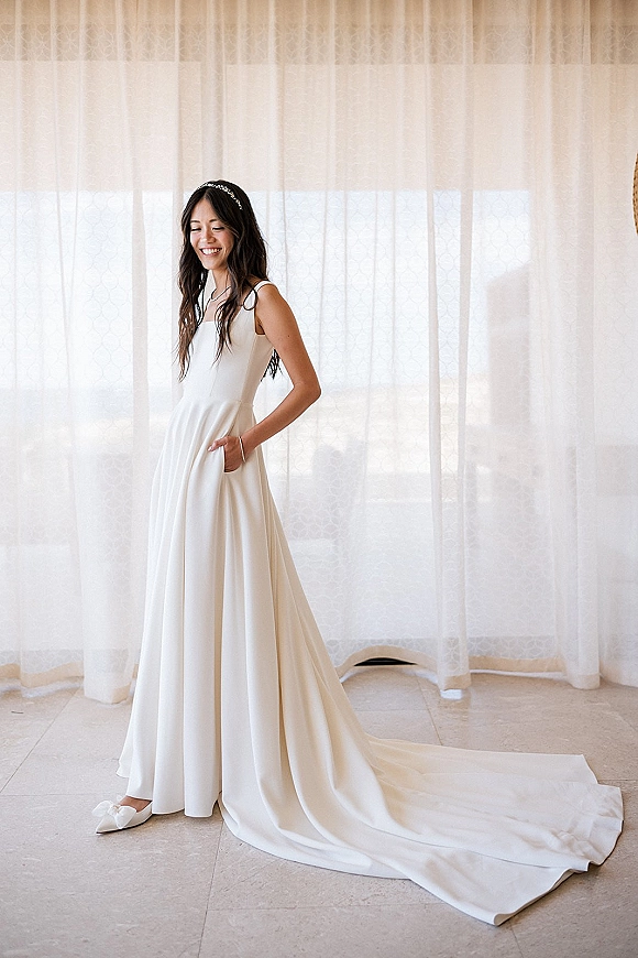 Bridal portrait of a bride in a minimalist wedding dress, full length with long train and pearl headband in soft window light indoors