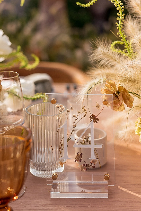 Wedding table number acrylic table numbers sign with pressed flowers and gold hardware on a wood outdoor reception tablescape with candles