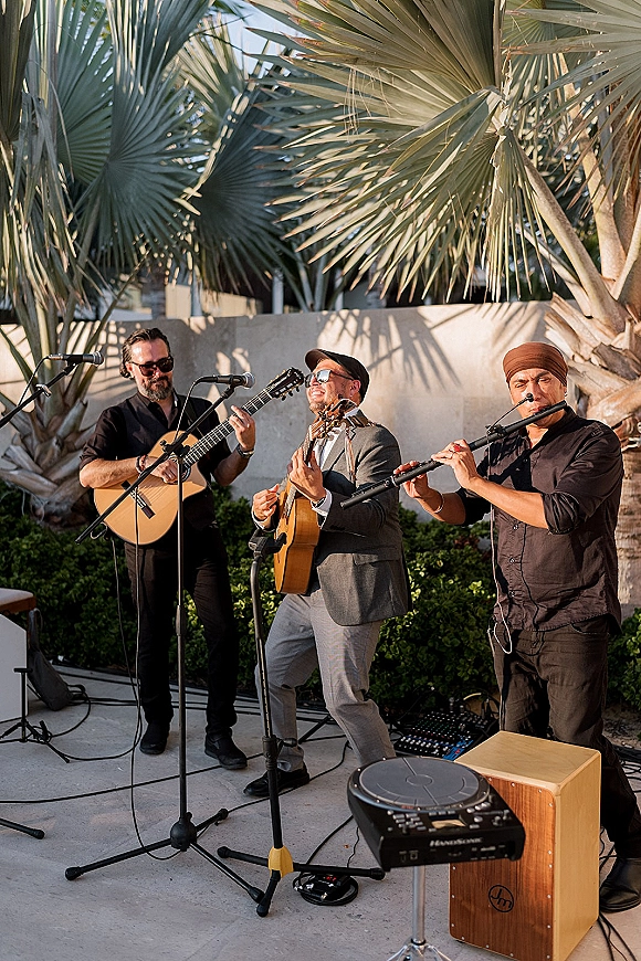 Wedding live band playing live music wedding reception on an outdoor patio with palm trees, microphones and acoustic guitars set up in front