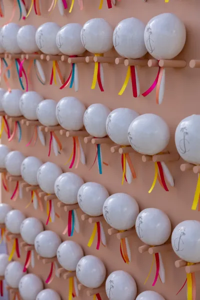Wedding favor display with white round monogram favors clipped to wooden pegs, colorful ribbon streamers hanging against a blush backdrop wall