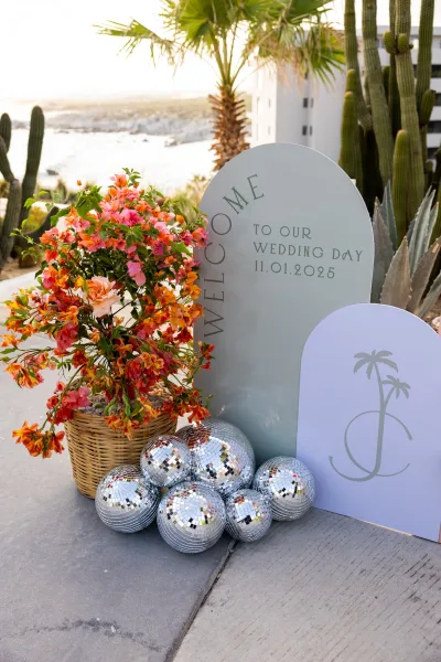 Wedding welcome sign with arched wedding welcome sign design, floral wicker basket and disco balls on a coastal walkway with palms and cacti