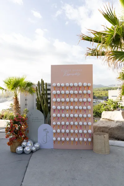 Wedding escort display with seating chart wall, acrylic signage and pampas grass on a patio with palm trees, blue sky, and ocean view