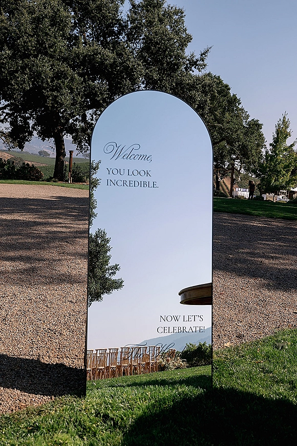 Wedding welcome sign, mirror welcome sign with calligraphy lettering on an easel along a gravel driveway with oak trees and distant hills