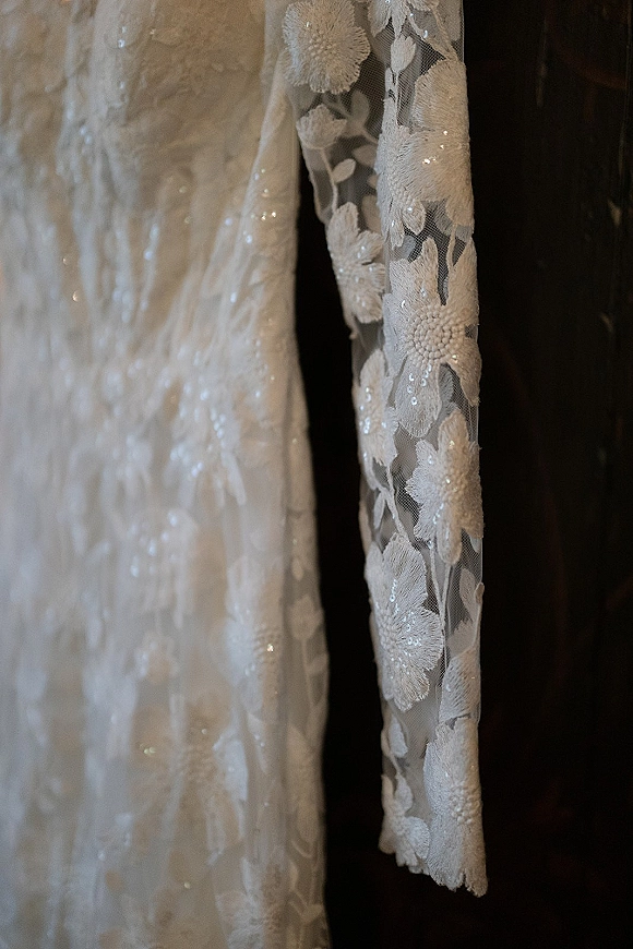 Wedding dress detail with lace wedding dress floral appliqué and beaded sequins on a sheer sleeve against a dark backdrop