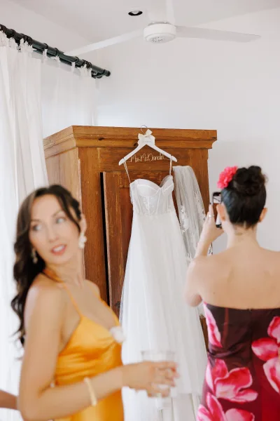 Wedding dress on a personalized wire hanger, strapless gown with lace bodice and tulle skirt hanging from a wooden armoire in window light