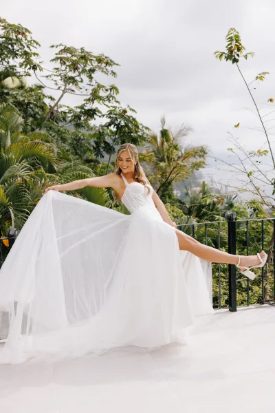 Bridal portrait of a bride in a corset wedding dress with a tulle skirt and train, holding it out on an outdoor terrace with tropical greenery