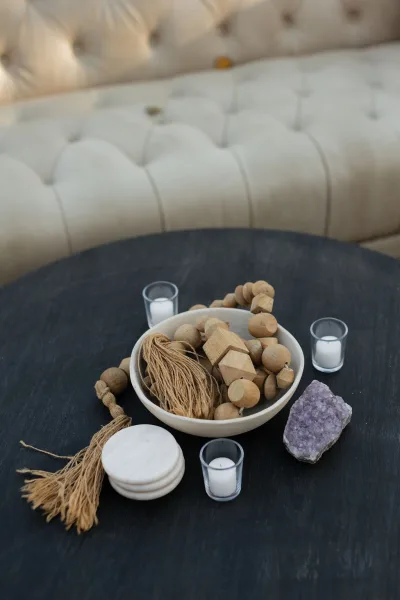 Coffee table decor with wooden beads on a dark round table, styled with votive candles, a bowl, tassel, and crystal near a tufted sofa