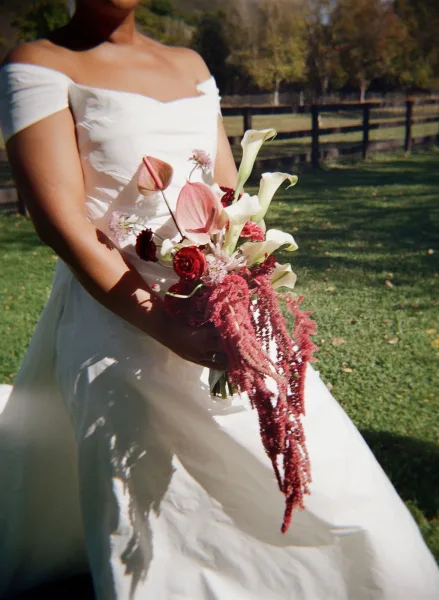 Bridal bouquet with cascading wedding bouquet design of calla lilies, anthurium, red roses, and amaranthus held outdoors by bride in sunlight