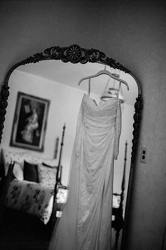 Wedding dress in an ornate mirror, lace wedding dress on a hanger beside a canopy bed in a softly lit bedroom suite