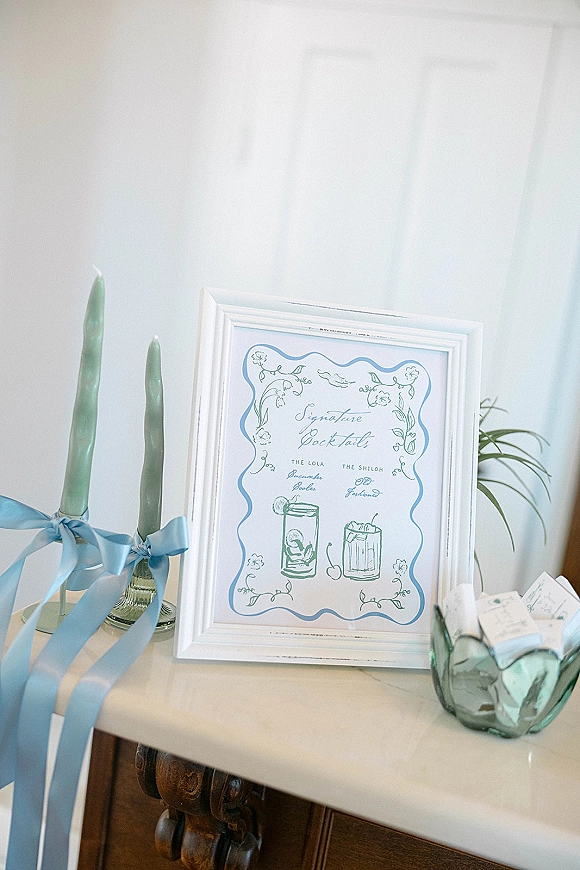 Wedding bar sign with signature cocktail sign in a white frame, styled with taper candles and blue ribbon bows on a tabletop setup