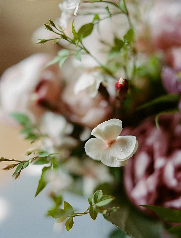 Bouquet close-up of white blossoms and blush pink roses with greenery and water droplets against a softly blurred background
