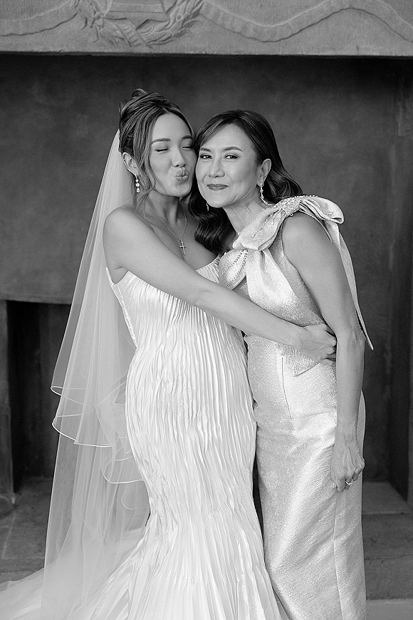 Bride and mother portrait with mother of the bride photo as they embrace by a stone archway, veil and one-shoulder gown in shade