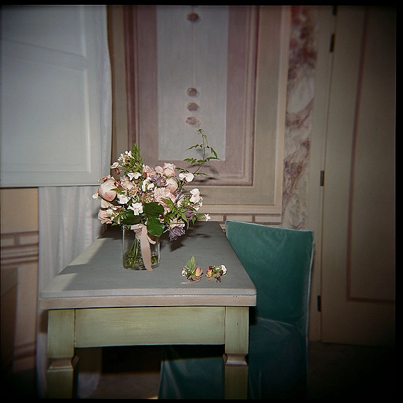 Wedding bouquet of blush pink and white flowers with greenery in a glass vase, ribbon and boutonniere on a painted wooden table indoors