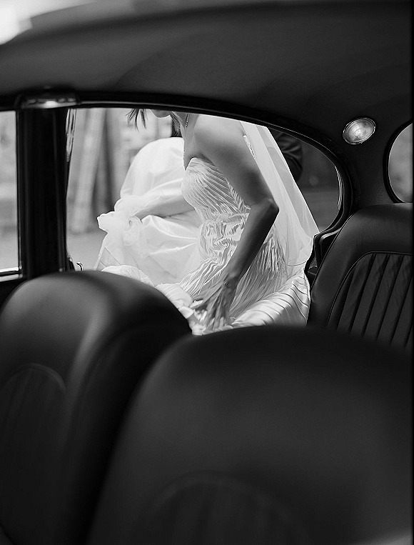 Bridal portrait of a bride in car, seated in a strapless wedding dress with veil over her shoulder, window light on leather seats