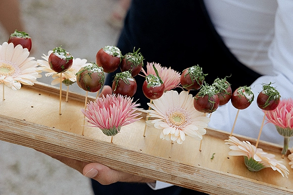 Wedding appetizers on toothpicks with cherry tomatoes and cream cheese filling on a wooden board, held on a tray with pink flowers