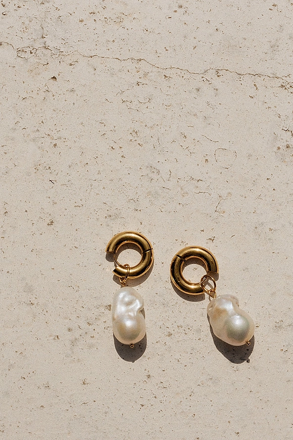 Pearl drop earrings with baroque pearls on gold hoop earrings, styled in a bridal jewelry flat lay on a textured stone surface