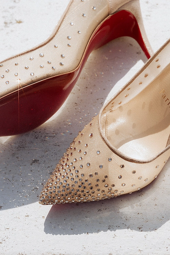 Wedding shoes with rhinestone wedding heels, pointed-toe nude mesh and red soles, resting on a light stone surface