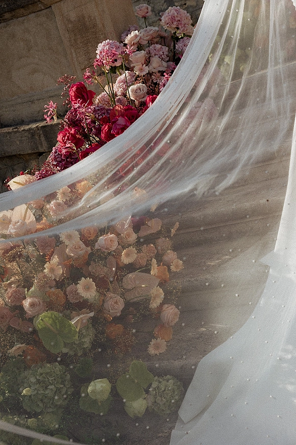 Wedding veil detail with pearl wedding veil tulle draped over roses and hydrangea arrangement on stone steps beside a stone wall