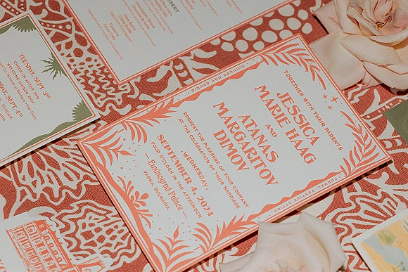 Wedding invitation suite with coral wedding invitations, envelopes and floral border on terracotta patterned textile with rose petals