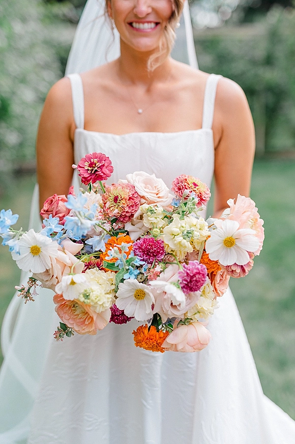 Bridal bouquet, colorful bridal bouquet of roses, zinnias, cosmos, and marigolds held by a bride in a white dress and veil outdoors