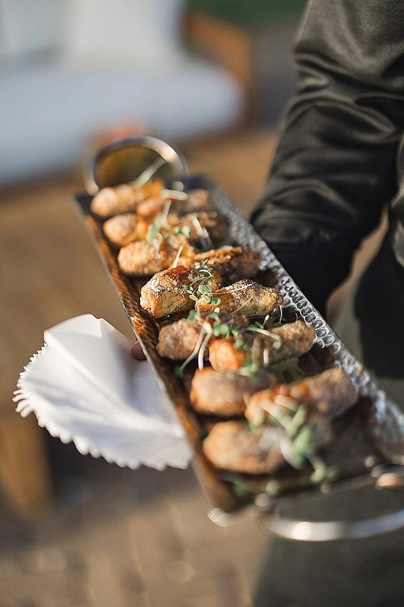 Wedding cocktail appetizers and wedding passed hors d'oeuvres on a metal tray with microgreens and toothpicks, carried outdoors in warm sunlight