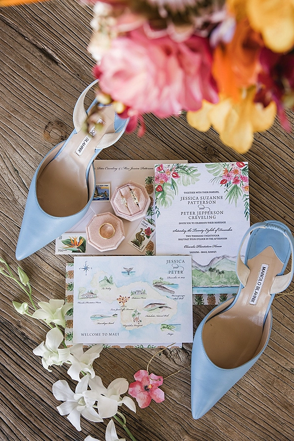 Invitation suite wedding invitation flat lay with illustrated map card, postage stamps, blue slingback heels, rings and tropical flowers on rustic wood floor