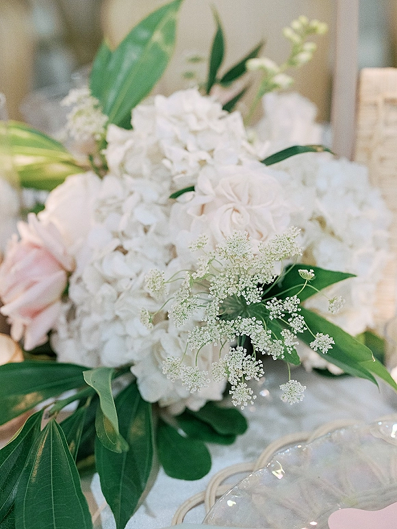 Bridal bouquet of white hydrangea bouquet blooms and blush roses with baby’s breath accents on a reception table beside a glass charger plate