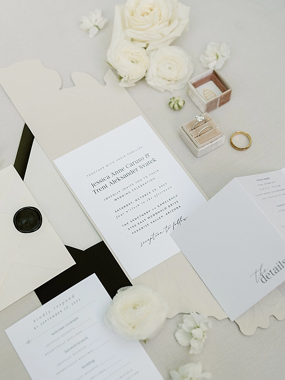 Wedding invitation suite with minimal wedding invitations, black wax seal, vellum wrap, rings in a box, and white roses on linen fabric