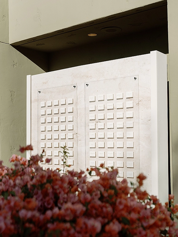 Seating chart display with wedding seating chart escort cards in acrylic frames on wall panels, accented by florals by a stucco entryway