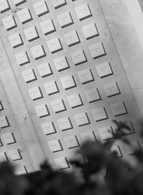 Seating chart with framed escort cards and printed names on a marble backdrop, with blurred greenery behind for a modern display
