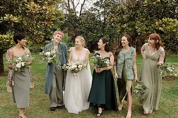 Wedding party portrait of a bride in a veil with bridesmaids holding bouquets, standing on a garden lawn with trees behind them
