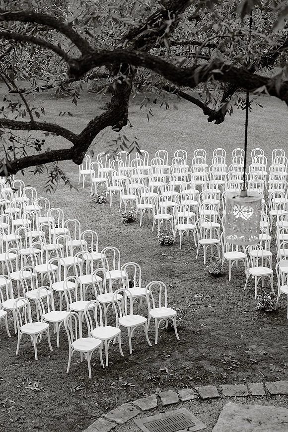 Ceremony seating with outdoor wedding ceremony chairs in neat rows, white chairs lining a floral aisle under tree branches and a hanging lantern