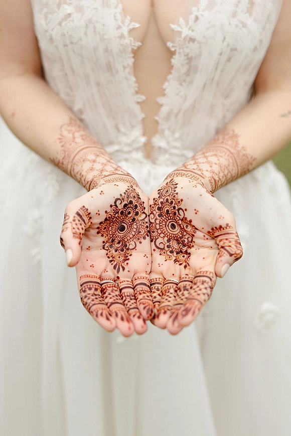 Bridal henna hands with mehndi designs cupped together, showcasing intricate palm patterns against a light neutral backdrop and lace bodice
