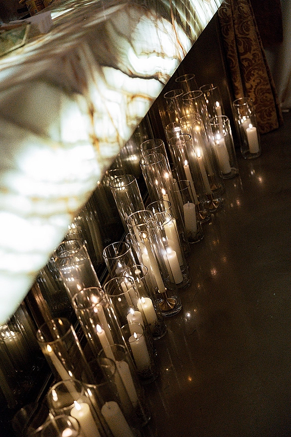 Wedding candle decor with glass cylinder wedding candles and white taper candles glowing on a dark tabletop against a stone wall backdrop