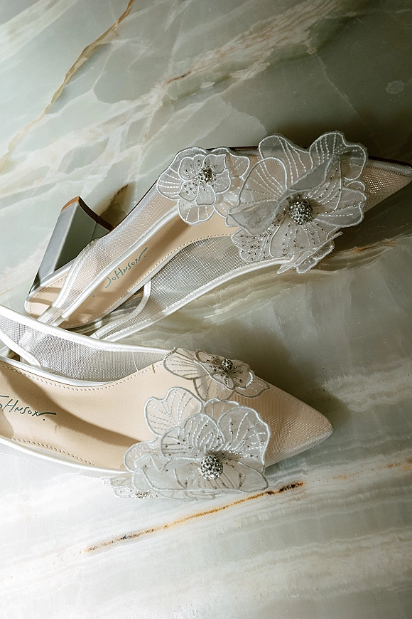Bridal shoes with wedding shoe detail, pointed toe heels in sheer mesh with 3D floral appliqués and beaded centers on marble surface
