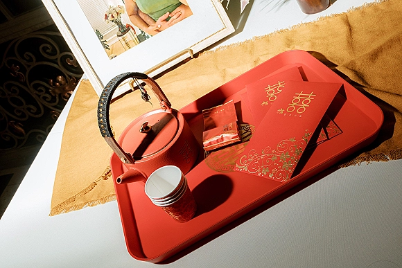 Wedding tea set on a red tea ceremony tray with teapot, cups, and red envelopes with gold lettering on a sunlit white tabletop