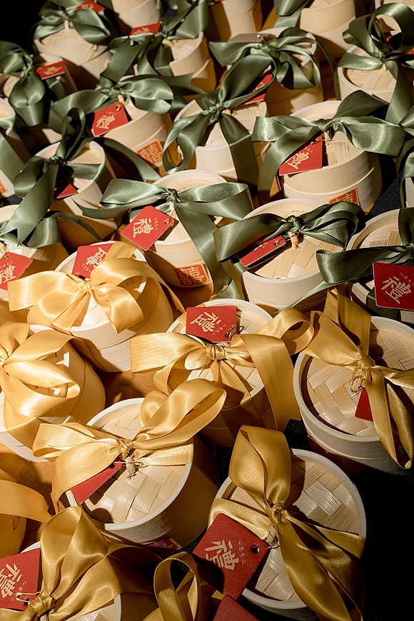 Wedding favor boxes arranged on a table, round bamboo boxes tied with satin ribbon bows and finished with red favor tags