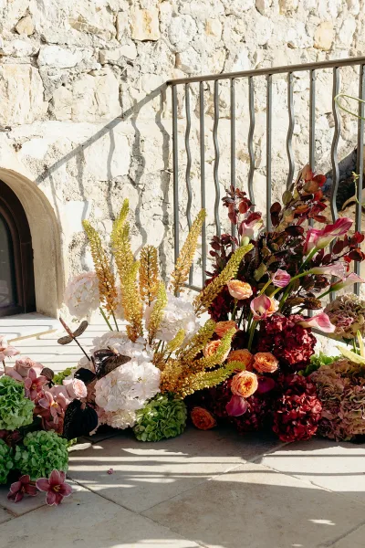 Wedding floral arrangement with calla lilies and hydrangeas, ceremony ground flowers spilling in front of an arched fireplace and stone wall