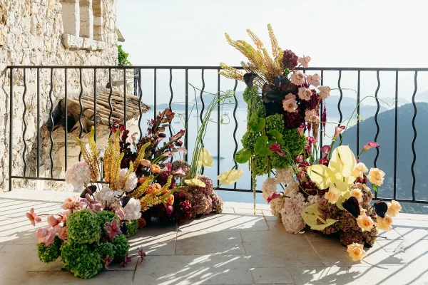Ceremony floral arrangement of hydrangeas, roses, calla lilies and anthurium with hanging amaranthus on a stone terrace overlooking the ocean